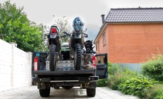 Rear view with two dirt bike motorcycles on the back of the camo truck with safety gear in residential setting.