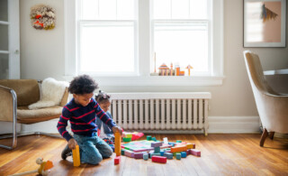 Two children play on wooden floor with colorful toys in front of white radiator
